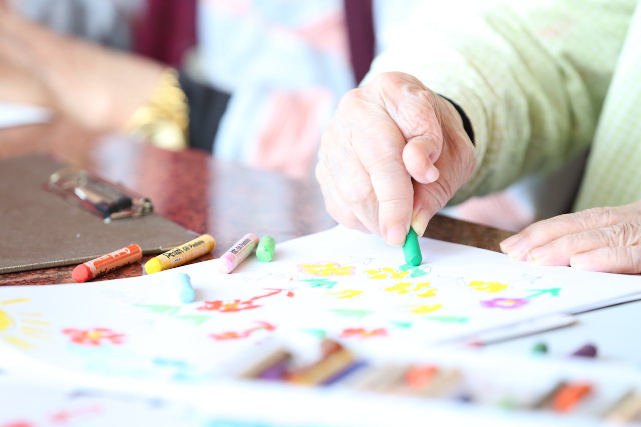 Close-up of a senior woman drawing with crayons in an art therapy session indoors.
